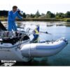 A man holding a rope attached to a dinghy that is suspended off a sailing boat using davit arms.